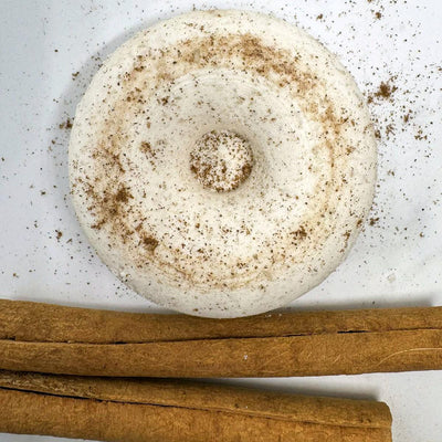 a white circular cinnamon shower steamer with decorative cinnamon sticks  