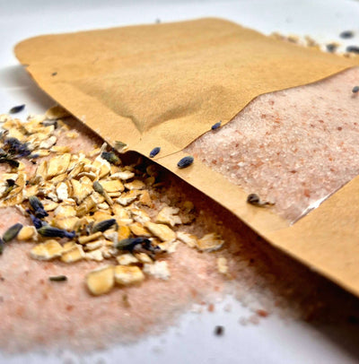 Oat bath salts spilling from a brown pouch, surrounded by oats and lavender for a relaxing bath experience.